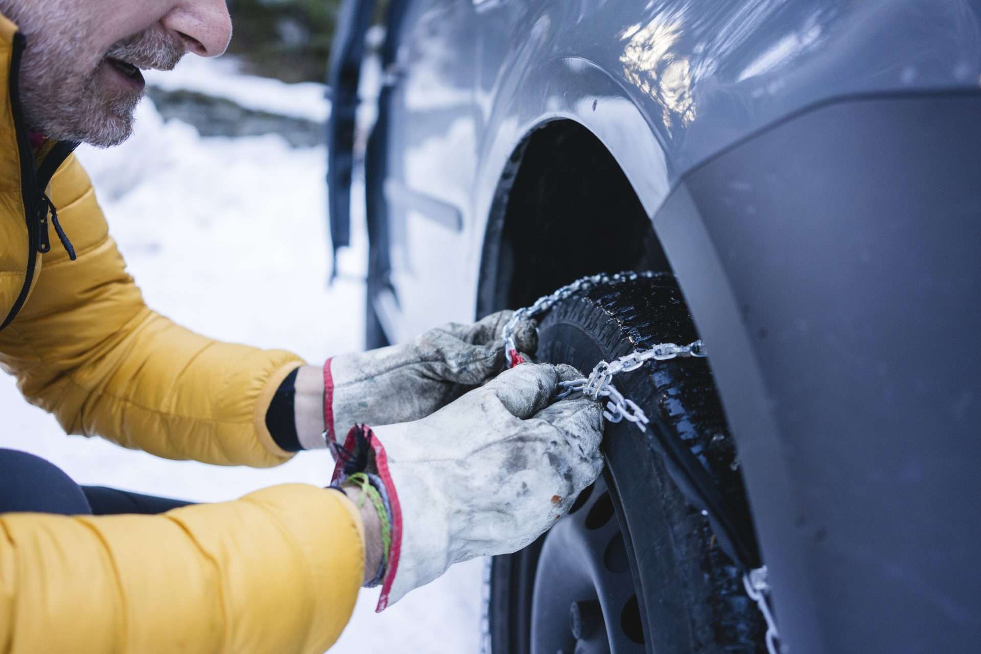 Man installing tire chains on tires in the snow