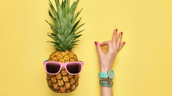 Pineapple with sunglasses on and hand holding up okay sign