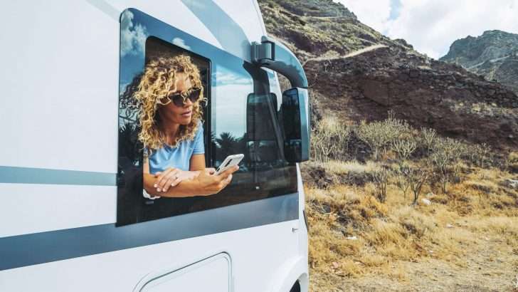 Woman leaning out RV window using phone to search for campsite