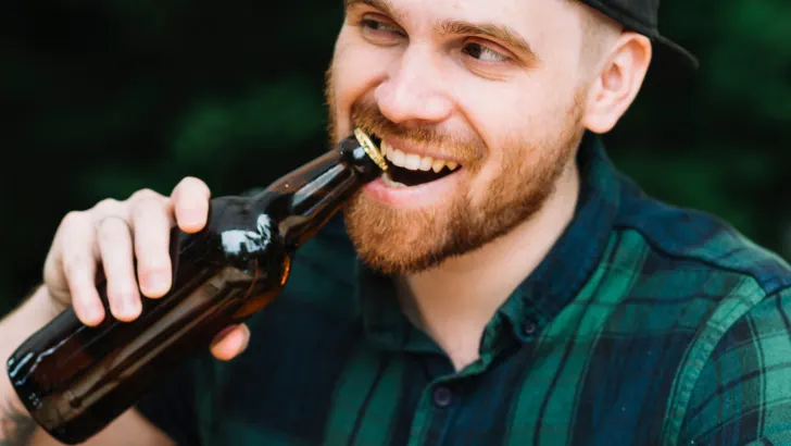 Man opening beer bottle with teeth
