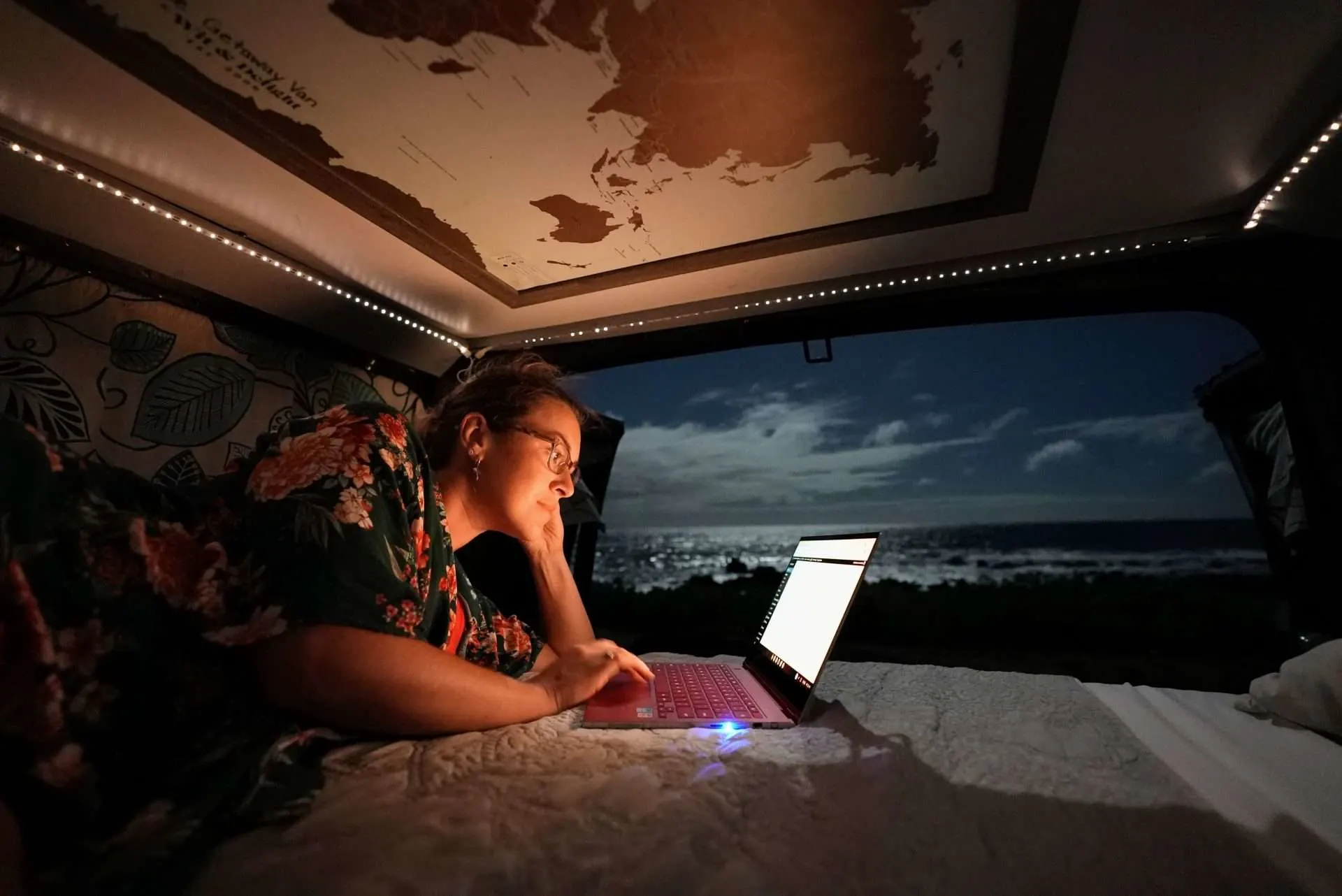 cait morton working on computer in camper van on the beach